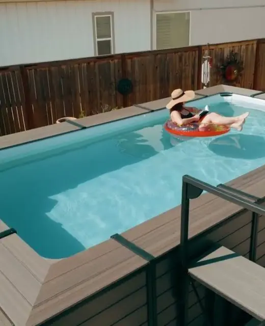 Person relaxing in above ground pool on a float, enjoying summer leisure in a backyard setting with wooden fence and sun hat.