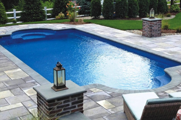 In-ground swimming pool with blue water, surrounded by stone patio, decorative lanterns, and landscaped greenery, showcasing a luxurious backyard setting for relaxation and entertainment.