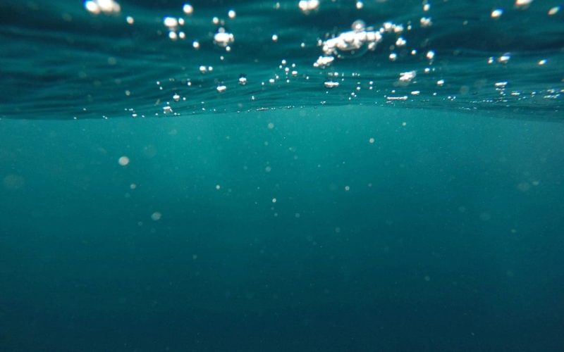 Underwater view with bubbles rising toward the surface, surrounded by deep blue water and dim light filtering from above.