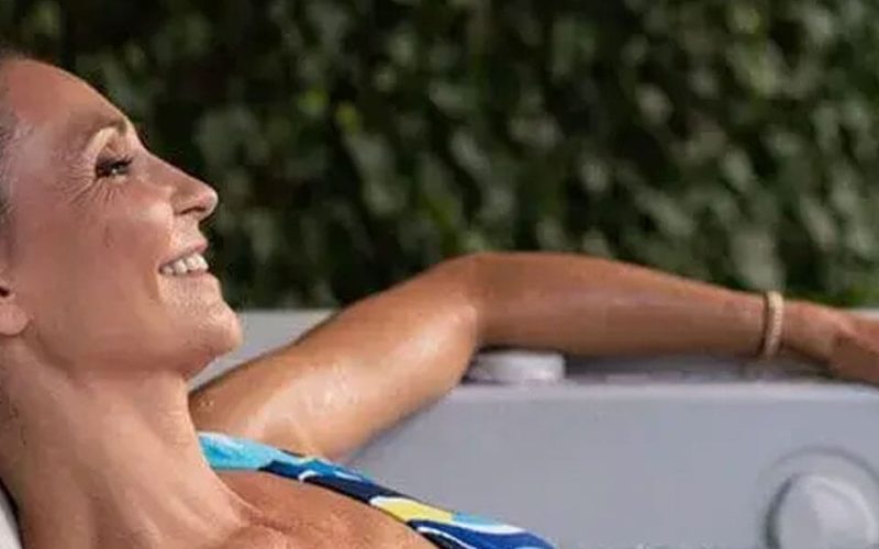 A woman in a colorful swimsuit relaxes and smiles while sitting in an outdoor hot tub, with greenery visible in the background.